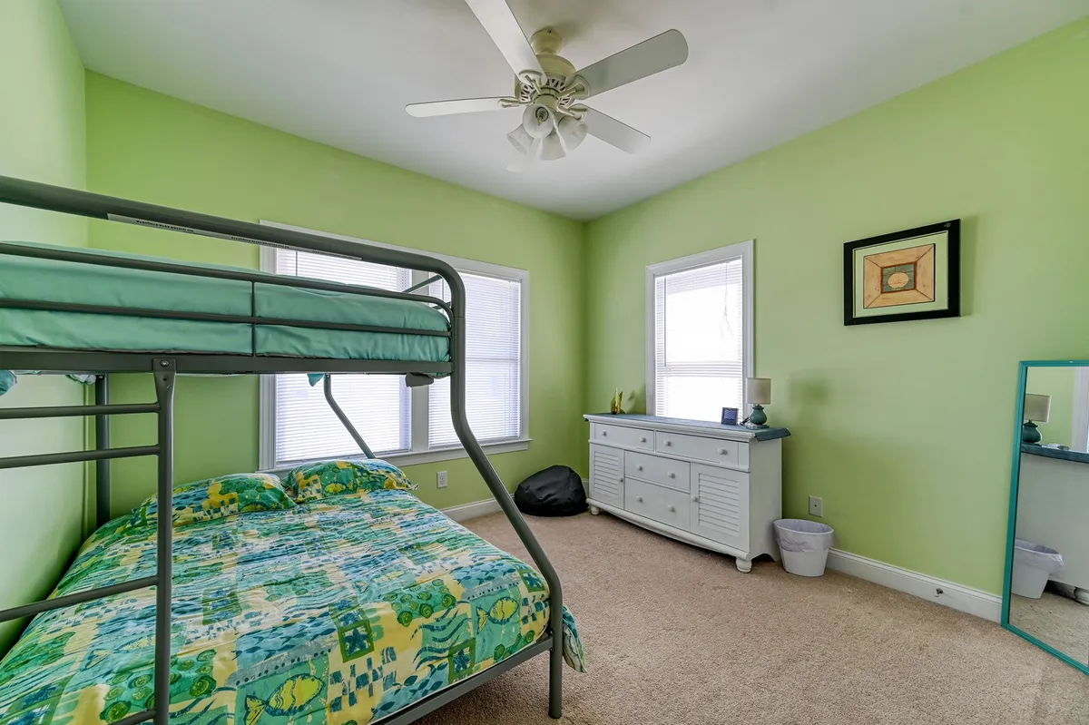 A playful bunkroom featuring a sturdy bunk bed with colorful bedding, a dresser beneath a window, and sunlight streaming into the space. The arrangement and pops of color evoke a fun, family-friendly vibe.