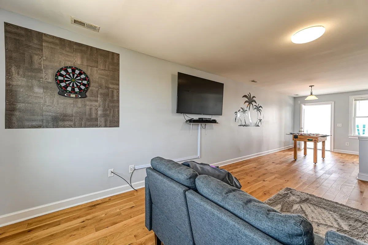 A bright, casual teen lounge showcasing a foosball table at center, an electronic dartboard mounted on the wall, and a fun palm tree mural. Large windows let in natural light, enhancing the energetic and playful vibe of the space.