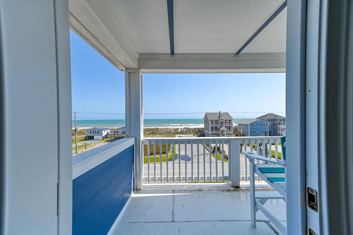 A tranquil scene from an outdoor balcony with comfortable seating and a stunning view of the ocean beyond the railing. The image evokes moments of quiet reflection, reading, or socializing while overlooking the water—embodying the relaxation and views central to the section.