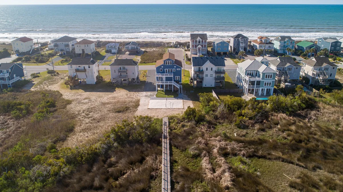 A walkway extends from beachfront houses directly to the sandy shoreline, with a sweeping view of the ocean. The setup evokes easy, spontaneous beach walks and group gatherings, highlighting the seamless connection between the property and the water.