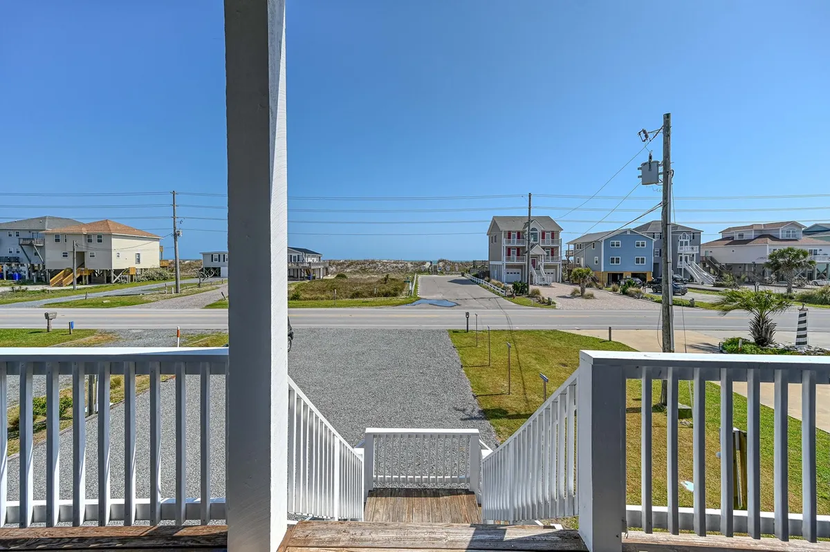 A wide view of the street and surrounding houses, framed by open sky. The scene hints at easy access to local walks, neighborhood exploration, and a welcoming outdoor environment. The perspective is open and inviting, suggesting proximity to the beach and dog-friendly strolls.