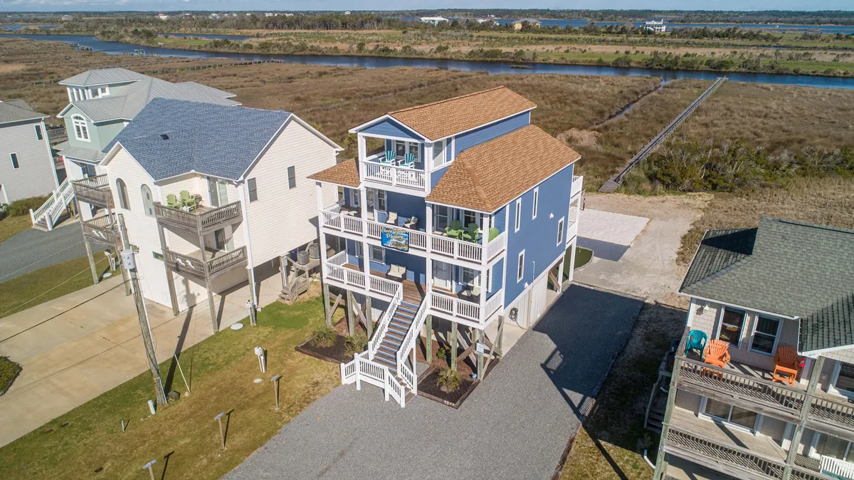 A broad view of the blue house, featuring the prominent staircase entryway and expansive decks on both levels. The image shows the house nestled in its landscape, highlighting the opportunities for family gatherings on the porch and the inviting transition from indoors to out.