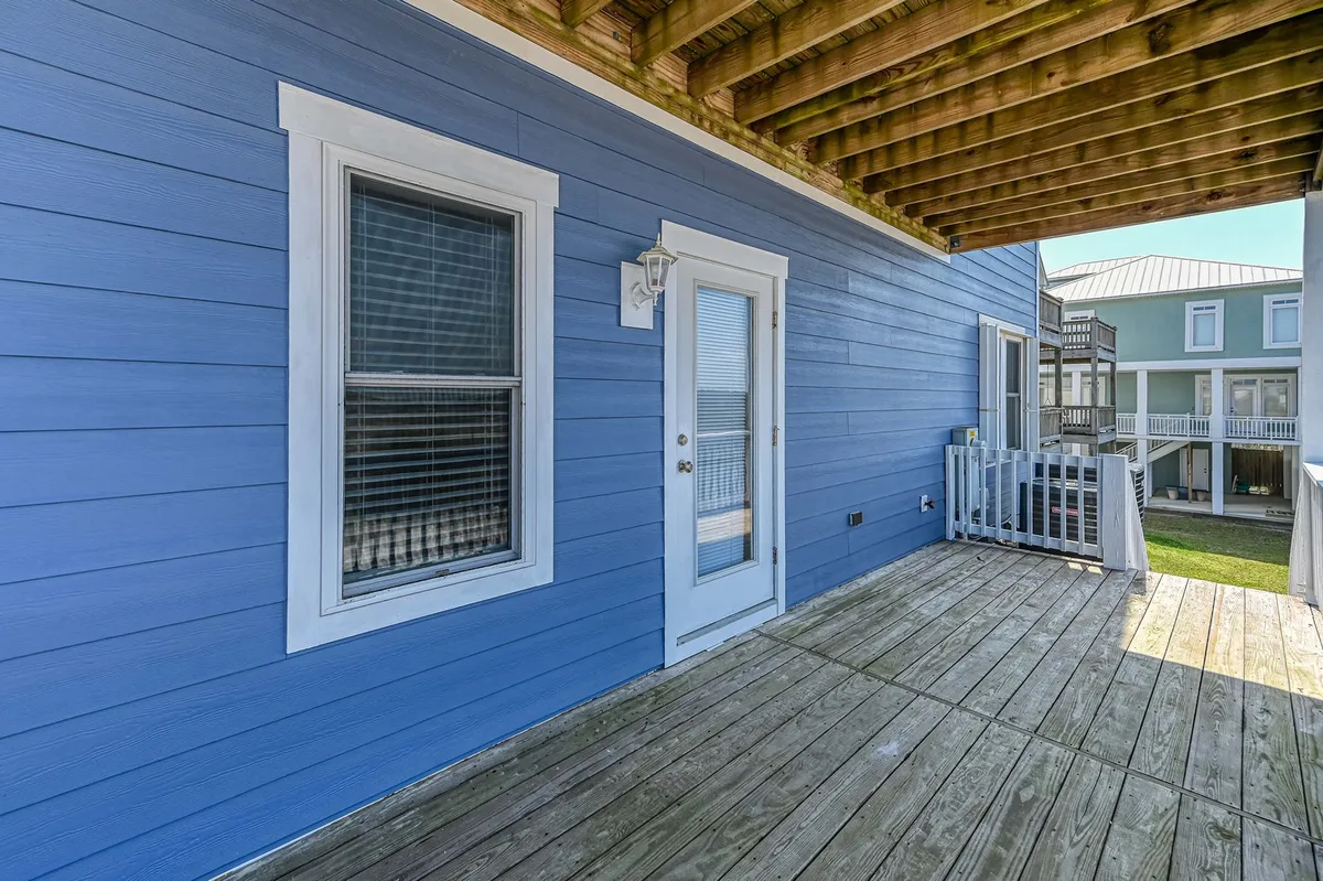 An exterior shot showcasing the blue siding and white trim of the house, with a wooden deck inviting guests to relax or gather. The cheerful, open mood suggests a great starting point or meeting place for setting out on island adventures or returning from them.