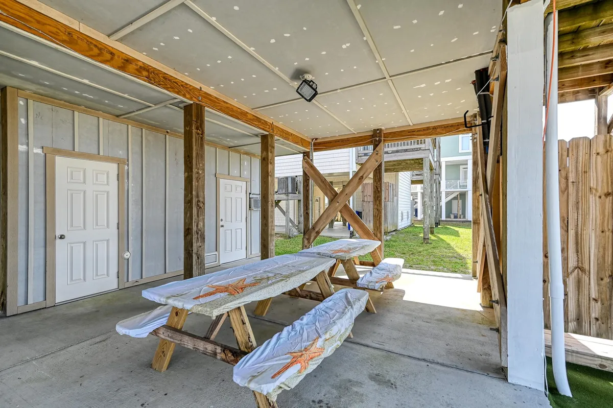 This image showcases a sunny, grassy backyard area with wooden picnic tables adorned with festive tablecloths. The space is open and bright, perfect for outdoor dining, relaxation, and play. The lush grass offers an inviting spot where dogs could romp and families can gather for meals or games.