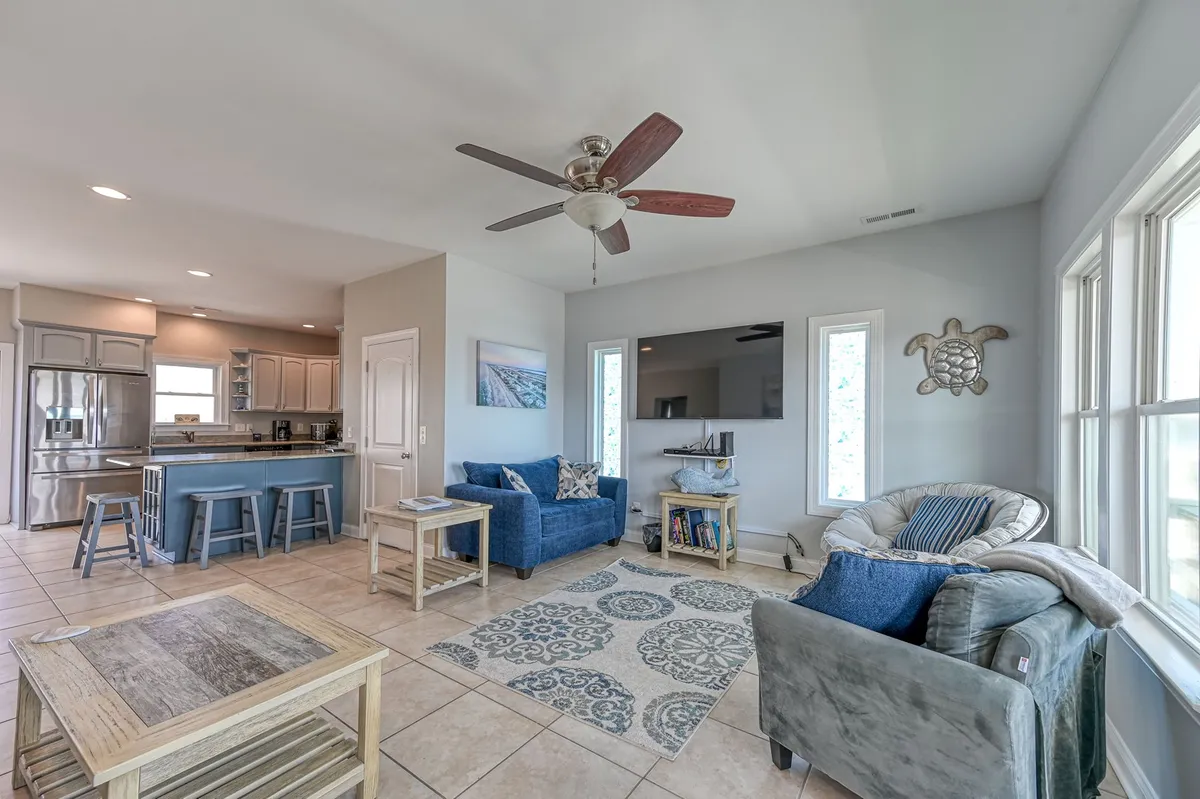 A casual living room scene featuring comfortable blue sofas and a decorative area rug. Large windows let in natural light, and the arrangement invites relaxation, conversation, and family movie nights. The space is both stylish and functional, supporting a variety of activities.