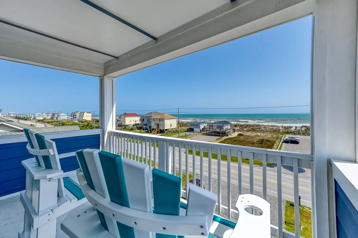 A pair of wooden chairs face a sweeping ocean view under a clear blue sky, suggesting a perfect setting for sunrise coffee or sunset drinks while soaking in the sea breeze.