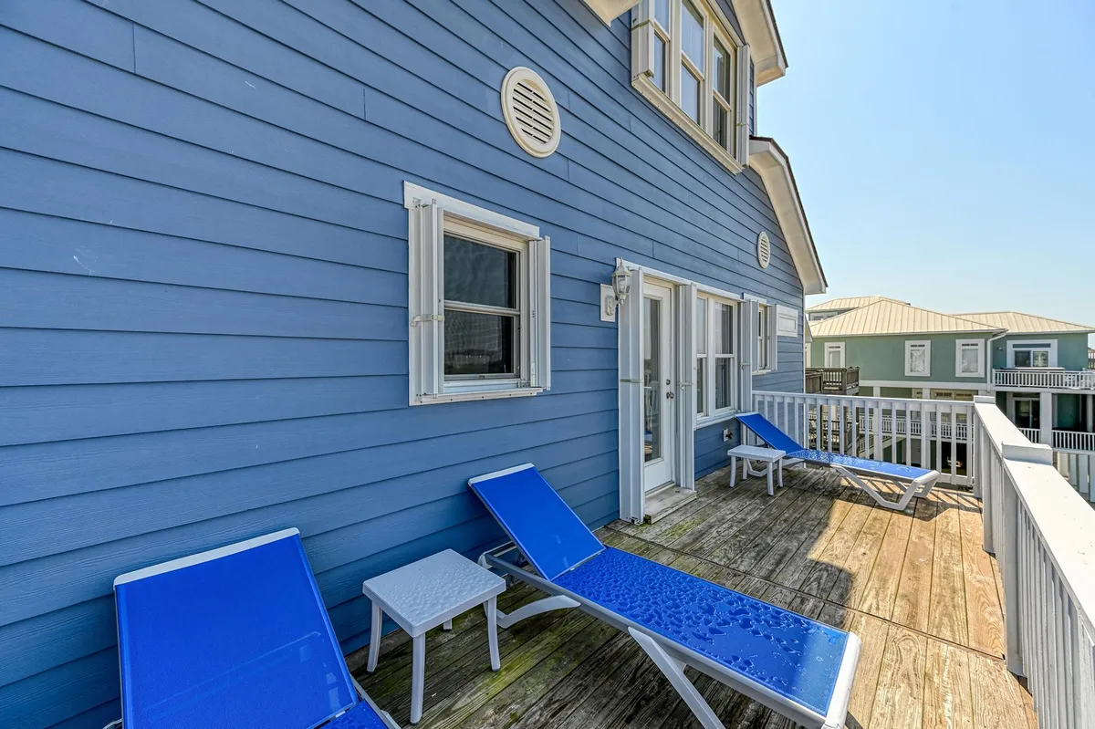 This image captures the front wooden deck of the blue house, furnished with lounge chairs and bathed in sunlight. The inviting exterior shows a space perfect for morning coffee, reading, or simply relaxing while taking in the views. The setup hints at both privacy and direct access to the outdoors, supporting the narrative of multi-generational relaxation zones.
