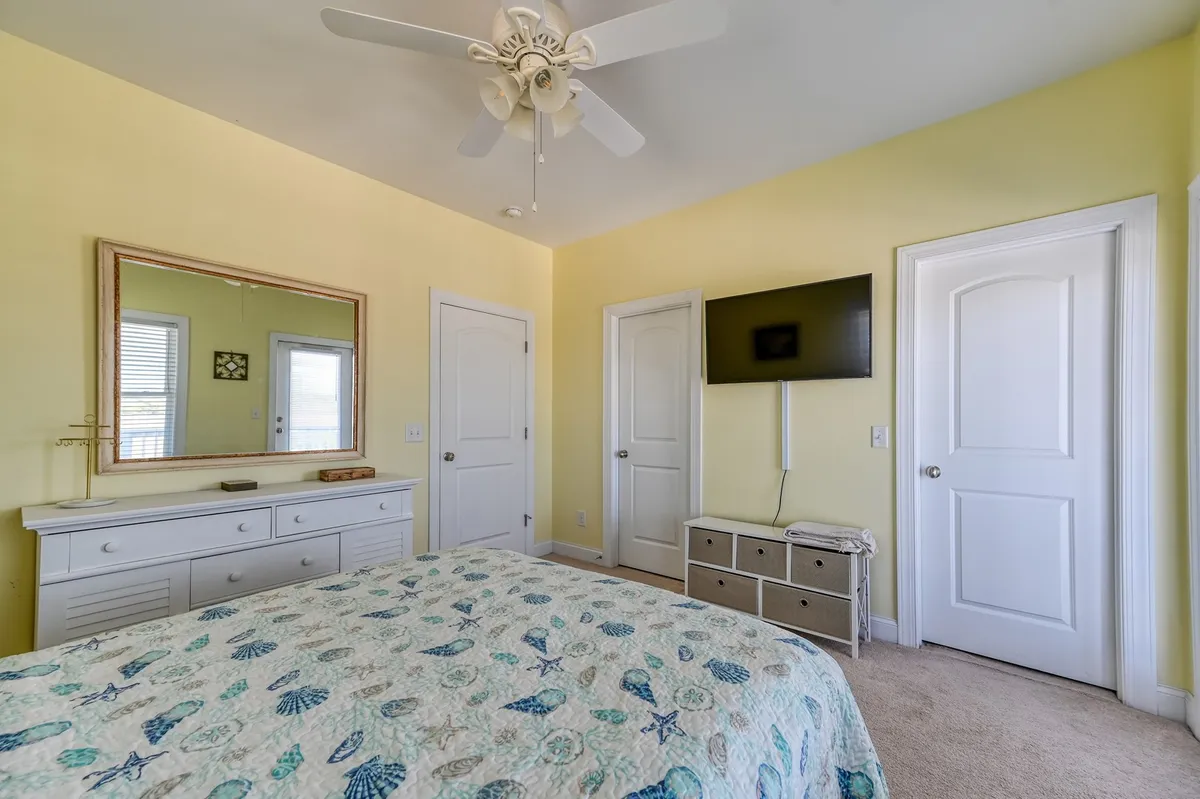 A serene bedroom with a patterned quilt bed, wall-mounted TV, a large dresser, and a mirror. Soft lighting and tranquil décor create a calm, restful atmosphere perfect for unwinding after a long day.