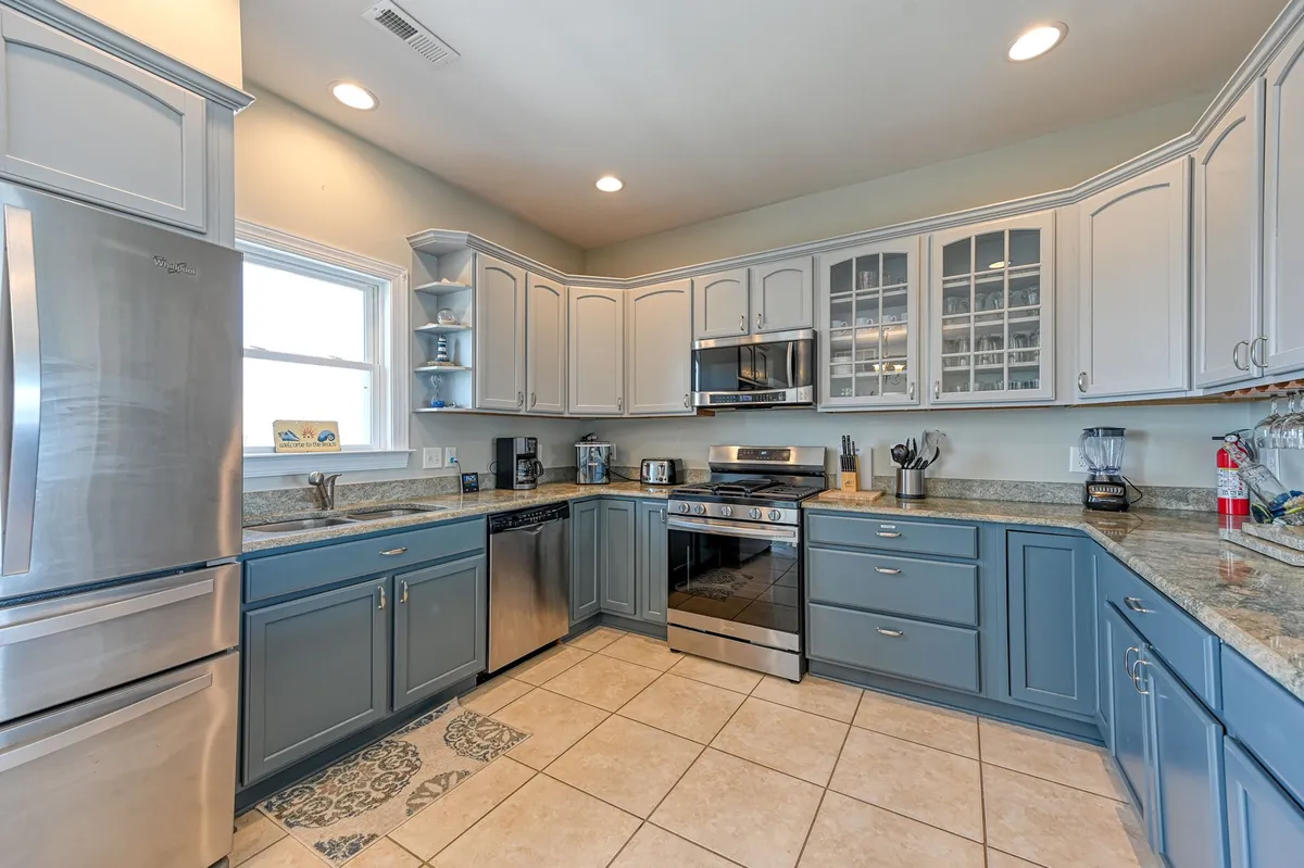 A beautifully appointed kitchen with stainless steel appliances, granite countertops, and striking blue cabinetry. The kitchen is spacious and designed for both functionality and style, with tile flooring enhancing the inviting atmosphere. Ample workspace and modern appliances make it ideal for preparing meals for family and entertaining guests.
